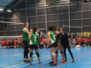 A group of ladies playing volleyball in a sports centre with a referee pointing in between them