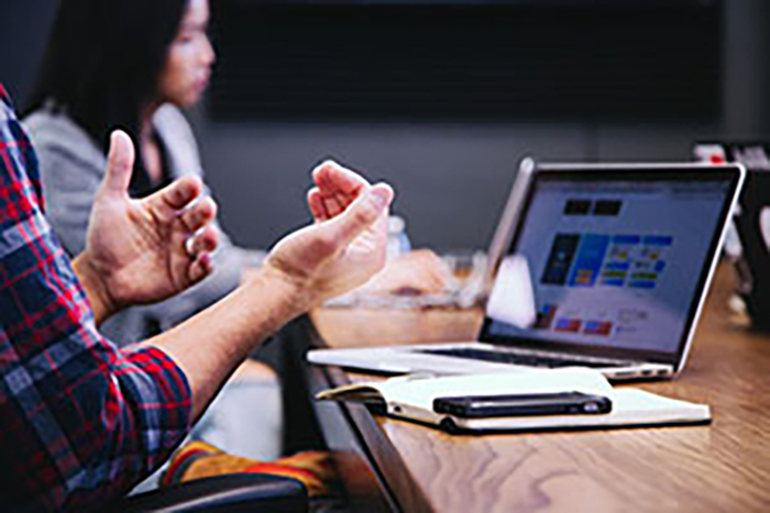A man’s hands and a woman looking at a laptop screen on a table with a notebook and pen