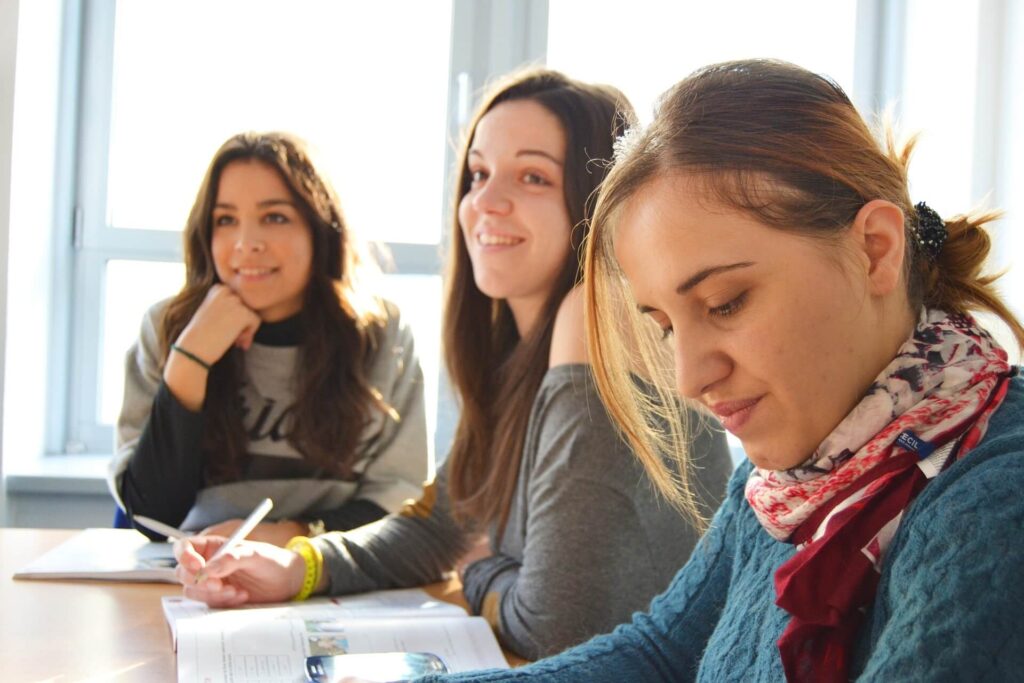 Three females sat at a desk reading from textbooks in a school lesson.